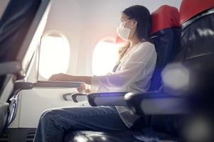 Young woman wearing face mask is using smartphone onboard, New normal travel after covid-19 pandemic concept photo