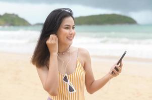 Young Beautiful woman in Bikini listening to music and using smartphone on the beach,  Summer, vacation, holidays, Lifestyles concept. photo