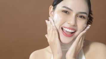 A young woman with beautiful face smiling, washing her face over brown background , beauty skin care concept photo