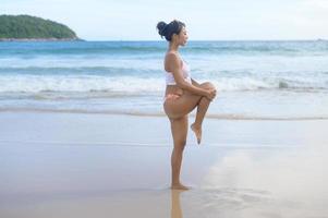 Young asian woman in bikini doing yoga on the beach, health and meditation concept photo