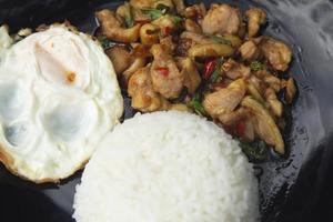 Basil, chicken, fried egg, Thai food The house style is not upscale in a black ceramic plate placed on a plaid concrete table. Ready to serve and delivery photo