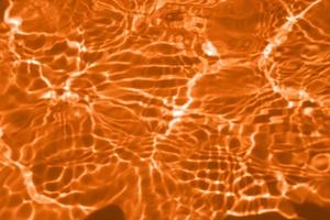 Defocus blurred transparent orange colored clear calm water surface texture with splashes and bubbles. Trendy abstract nature background. Water waves in sunlight. Calm orange water background. photo