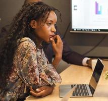 Black businesswoman attending business strategy meeting. Creative young woman listening to colleague addressing startup project meeting in modern office. Brainstorming, collaboration concept. photo