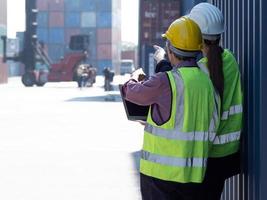 Industrial engineer and foreman worker working together inspecting container box at commercial shipping yard. Logistic manager checking, examining cargo boxes at import export distribution warehouse photo