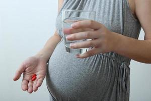 Pregnant woman drinking some water with medicine photo