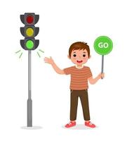 cute little boy holding go sign near pedestrian traffic light with indicator green light on vector