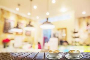 Two coffee cups on brown wooden table over blurred photo of beautiful coffee shop for background use