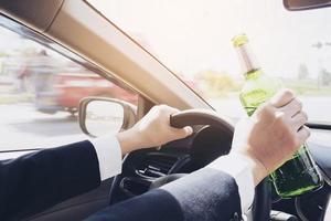 hombre sosteniendo una botella de cerveza mientras conduce un automóvil foto