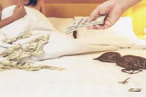 Man paying money dollar to prostitute woman on white bed in hotel photo