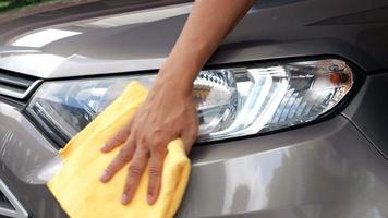 La main au ralenti 4k d'un employé utilise un chiffon jaune propre pour essuyer la voiture après le lavage dans l'atelier de lavage de voiture