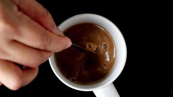 bovenaanzicht slow motion videobeeld van de hand van een vrouw die hete koffie zet in een witte mok op zwarte achtergrond-4k video
