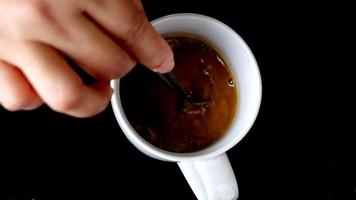 immagine video al rallentatore vista dall'alto della mano di una donna che prepara caffè caldo in una tazza bianca su sfondo nero-4k