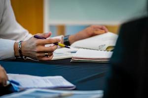 cerca de la mano del hombre, sostiene un bolígrafo morado y se concentra para escuchar al profesor mientras abre el manual en la mesa. foto