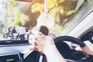 Man is dangerously holding cup of cold drink while driving a car photo