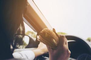 Lady driving car while eating hamburger photo