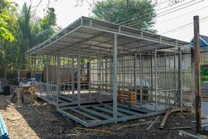 La pequeña casa temporal de la criada en construcción está hecha de estructura de postes de acero sin cemento y ladrillo con jardín y cerca alrededor. foto