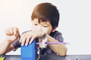 A boy is sharpening his pencil using mechanical sharpener over white background photo