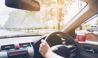 Man driving car using one hand while holding a coffee cup in other hand photo