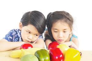 niño y niña asiáticos que muestran una expresión de desagrado con verduras frescas y coloridas aisladas sobre fondo blanco foto