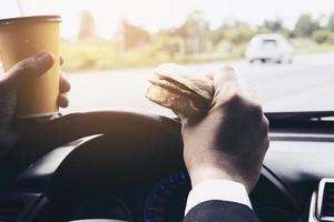 Man driving car while holding a cup of cold coffee and eating hamburger photo