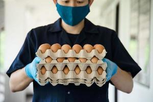 un hombre lleva una bandeja de huevos de 3 capas para mantenerse seguro en casa poniendo guantes sanitarios durante la propagación del virus corona covid-19 - personas que mantienen alimentos en el concepto de período de propagación viral covid-19. foto