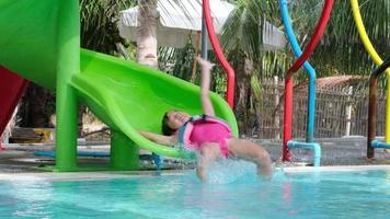 kind op waterglijbaan bij aquapark. klein meisje met plezier bij het zwembad. zomervakantie. video