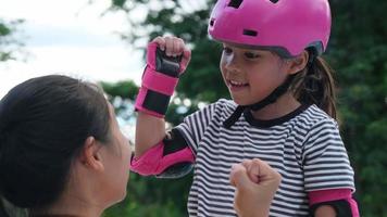 Loving mother helping her daughter to playing roller skate in the park. Mother encourages daughter to practice roller skating. Exciting outdoor activities for kids video