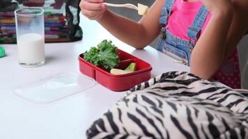retrato de una colegiala sentada en una mesa y comiendo alimentos saludables durante el descanso en la escuela. comida para el almuerzo, loncheras con sándwiches, frutas, verduras y leche. video