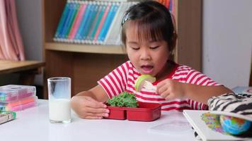 retrato de una colegiala sentada en una mesa y comiendo alimentos saludables durante el descanso en la escuela. comida para el almuerzo, loncheras con sándwiches, frutas, verduras y leche. video