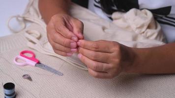 Hand of a seamstress threading a needle, close up. Mother sews a beautiful dress for her little daughter by hand.