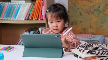 linda niña sosteniendo un lápiz óptico trabajando en una tableta. niño que usa una tableta digital buscando información en Internet para su tarea, educación en el hogar, educación en línea de aprendizaje electrónico. video
