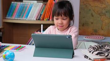 linda niña sosteniendo un lápiz óptico trabajando en una tableta. niño que usa una tableta digital buscando información en Internet para su tarea, educación en el hogar, educación en línea de aprendizaje electrónico. niño moderno video