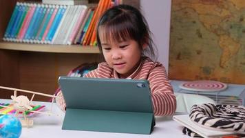 schattig klein meisje met een styluspen die aan een tablet werkt. kind dat digitale tablet gebruikt om informatie op internet te zoeken voor haar huiswerk, thuisonderwijs, e-learning online onderwijs. video