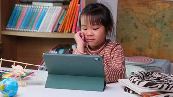 linda niña sosteniendo un lápiz óptico trabajando en una tableta. niño que usa una tableta digital buscando información en Internet para su tarea, educación en el hogar, educación en línea de aprendizaje electrónico. video