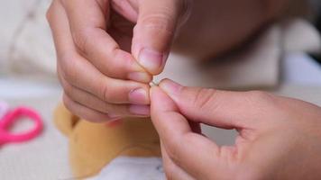 hand van een naaister die een naald inrijgt, close-up. moeder naait met de hand een mooie jurk voor haar dochtertje. video