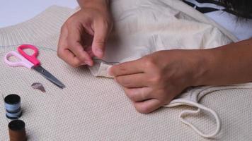 main d'une couturière au travail avec du tissu en tissu. mère coud une belle robe pour sa petite fille à la main, gros plan. la main de femme coud des coutures avec des fils bleus. video