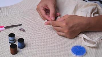 main d'une couturière au travail avec du tissu en tissu. mère coud une belle robe pour sa petite fille à la main, gros plan. la main de femme coud des coutures avec des fils bleus. video