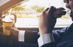 Man driving car while holding a cup of cold coffee and eating hamburger photo