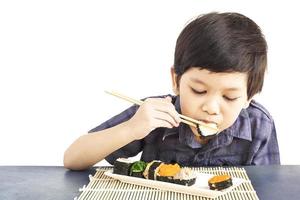 Asian lovely boy is eating sushi over white background photo