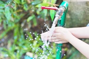 el niño se está limpiando la mano en el agua de la pestaña del suelo del campo de la escuela foto