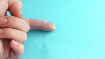 ein Tropfen der Universallösung tropft auf die Kontaktlinse, die auf dem Finger des Mannes liegt. Kontaktlinsen reinigen und waschen
