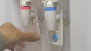 mano maschile che serve acqua calda di un refrigeratore d'acqua in un bicchiere di plastica. video