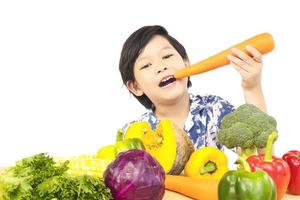 niño sano asiático que muestra una expresión feliz con una variedad de verduras frescas y coloridas sobre fondo blanco foto