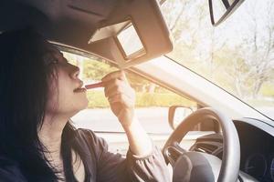 Woman making up her face using lipstick while driving car, unsafe behavior photo