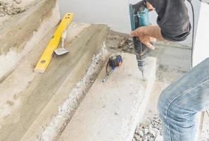 Partial focus of a man is working with reinforce concrete stair structure modification using hand drill machine in construction site photo