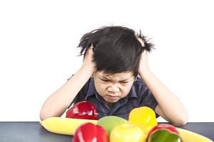 Asian boy is showing dislike vegetable expression over white background photo