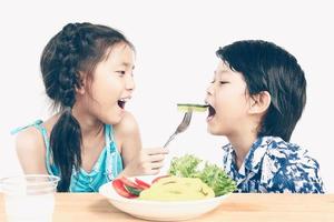 Vintage style photo of asian boy and girl are happily eating fresh vegetable salad with a glass of milk isolated over white background