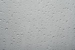 Rain drop on at glass window over gray sky background photo