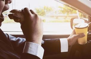 Man driving car while holding a cup of cold coffee and eating hamburger photo