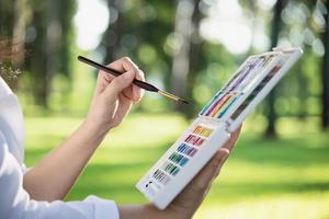 relájese mujer pintando obras de arte de color de agua en la naturaleza verde del bosque del jardín - personas con arte creativo en la naturaleza reducción del estrés y concepto de meditación foto